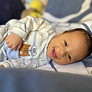 Gabriele is registered to the contest to win money with this photo: baby, smiling, pajamas, striped_clothing, bed, blanket, infant, cute, face, child, happy, lying_down, soft_toys, cozy, indoors, person, young_child, head, sleepwear, resting