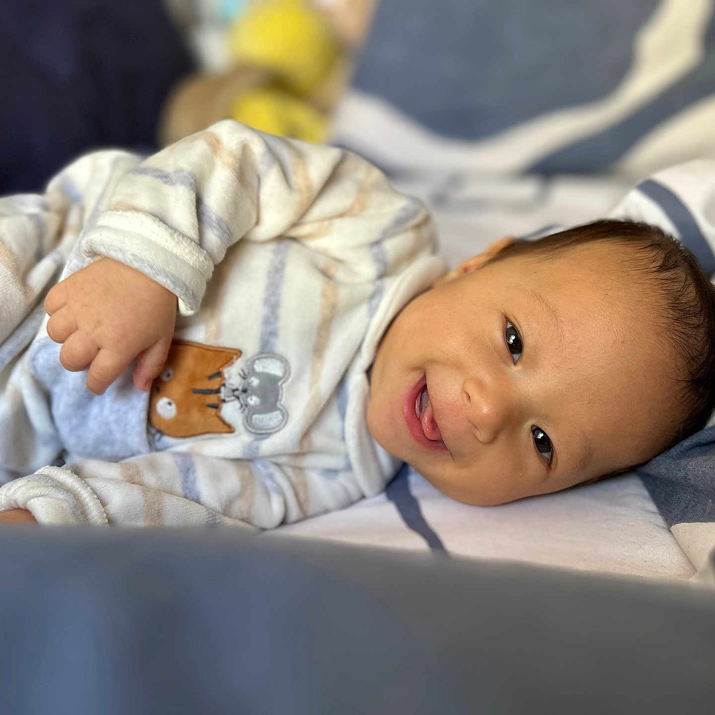Gabriele is registered to the contest to win money with this photo: baby, bed, blanket, child, cozy, cute, face, happy, head, indoors, infant, lying_down, pajamas, person, resting, sleepwear, smiling, soft_toys, striped_clothing, young_child