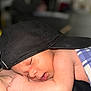 baby, sleeping, cap, black_cap, blanket, blue_checkered_blanket, skin, face, arm, hand, person, closeup, soft_focus, indoor, newborn, tender_moment, resting, peaceful, portrait, candid