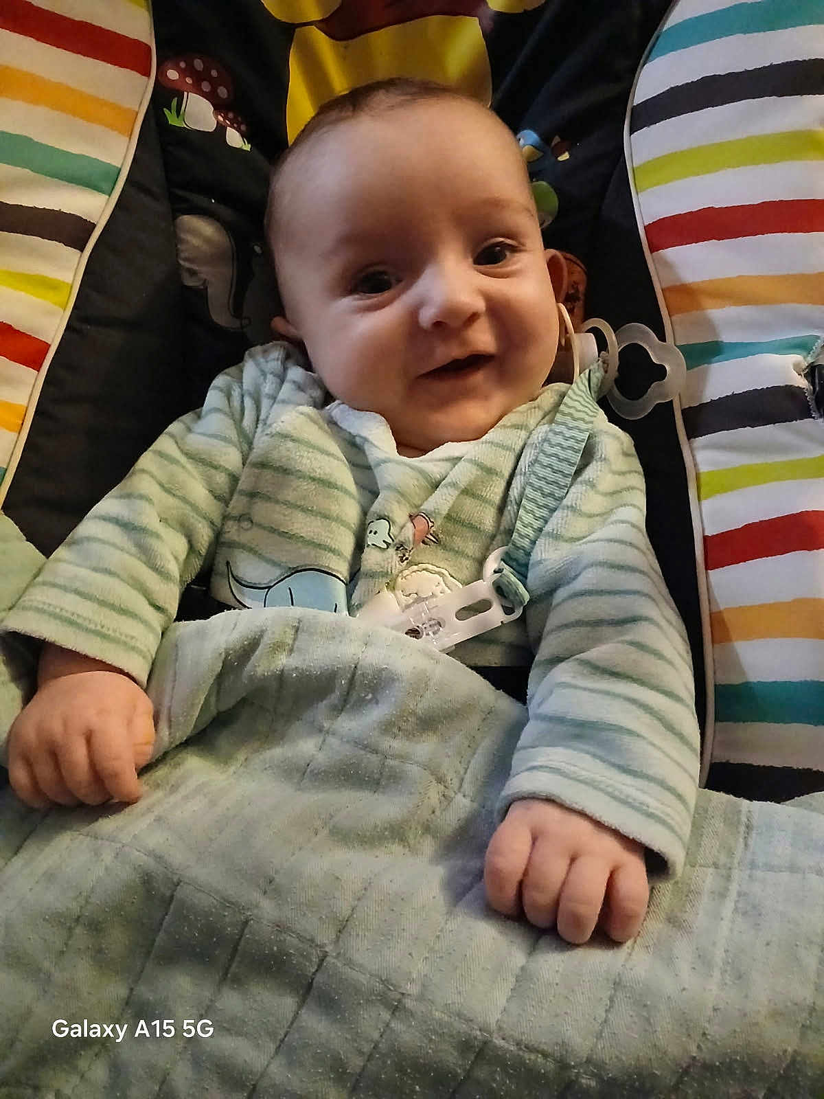 Nolan a rejoint le concours — aidez-le/la à gagner de superbes lots ! baby, infant, smiling, face, hands, blanket, onesie, pacifier_clip, baby_seat, striped_pattern, buckle, cloth, indoor, cozy, close_up, portrait, young_child, happy, soft_lighting, mushroom_pattern