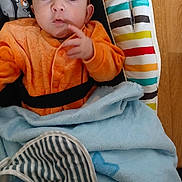 Nolan participe au concours pour gagner de l'argent avec cette photo : baby, infant, child, onesie, orange_clothing, blue_blanket, striped_cushion, bouncer_seat, face, eyes, hand, wooden_floor, portrait, indoor, blanket, curious_expression, camera_watermark, closeup, fabric, relaxed