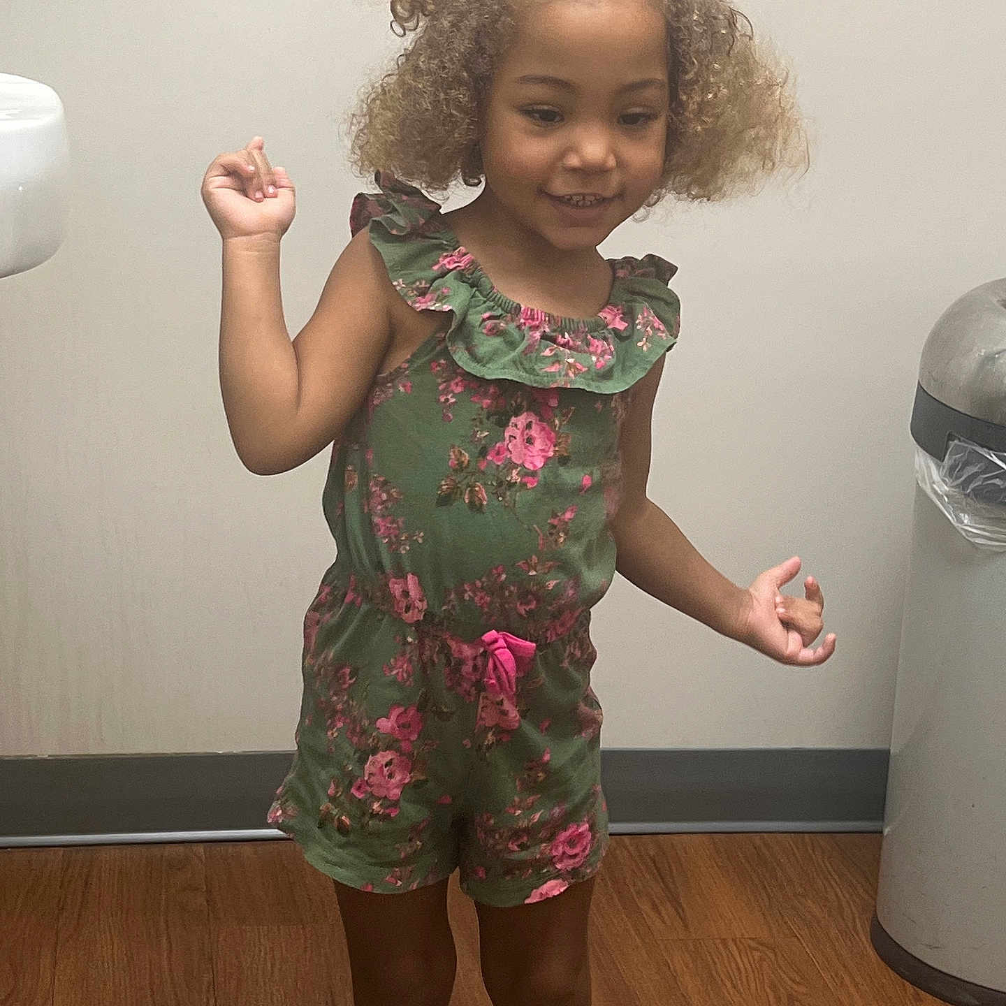 Azylah is registered to the contest to win money with this photo: casual, child, curly_hair, cute, floral_pattern, girl, green_clothing, happy, human, indoor, person, playful, romper, shorts, skin, smiling, standing, trash_can, wooden_floor, young