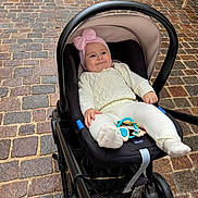 Miia a rejoint le concours — aidez-le/la à gagner de superbes lots ! baby, stroller, infant, pink_hat, white_clothing, cobblestone, outdoor, smile, child, seat, toy, footwear, person, cute, knitwear, headwear, expression, wheels, hand, cozy