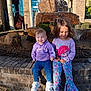 children, kids, smiling, fountain, rock, water, brick, outdoor, daylight, clothing, hoodie, pants, shoes, building, plants, happy, two_people, sitting, casual, young