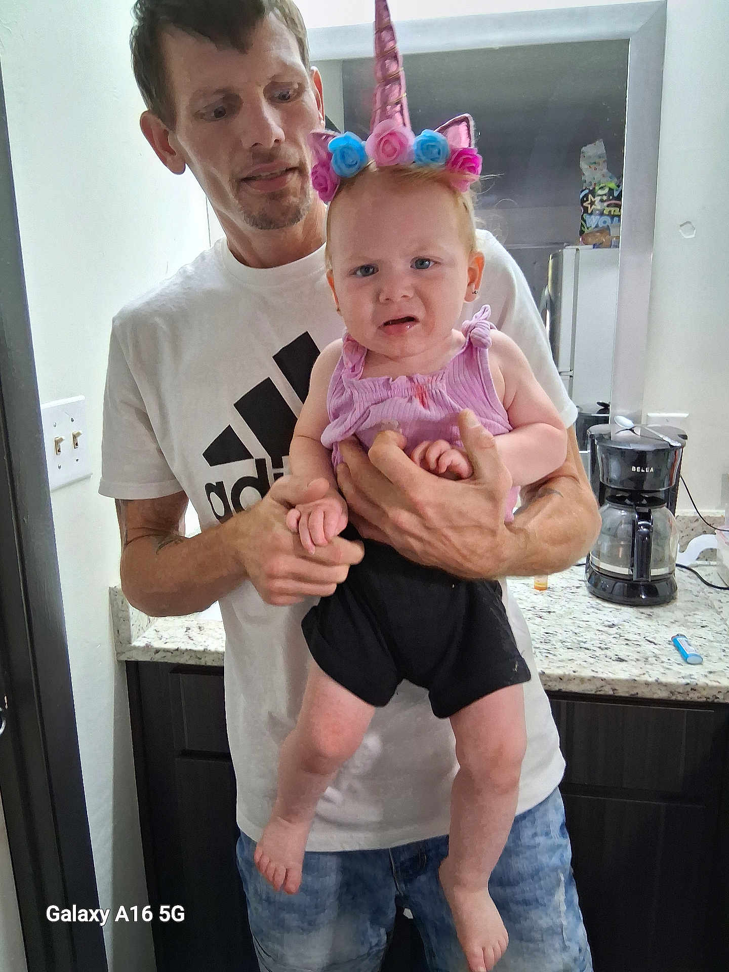 Braelon joined the competition — help win amazing prizes! man, baby, unicorn_headband, pink_top, black_shorts, kitchen, coffee_maker, mirror, counter, holding, upset_expression, casual_clothing, indoor, person, portrait, home, cabinet, light_switch, jeans, facial_expression