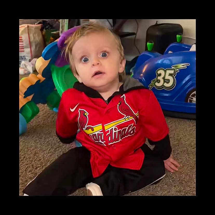 Cooper joined the competition — help win amazing prizes! child, toddler, red_jersey, cardinals, sitting, carpet, toy_car, blue_toy, indoor, curious_expression, blonde_hair, person, casual_clothing, floor, playroom, young_child, wide_eyes, home, portrait, cute