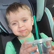 Cooper is registered to the contest to win money with this photo: toddler, child, car_seat, cup, straw, green_shirt, light_hair, blue_eyes, face, hand, seat_belt, car_interior, young_child, portrait, expression, drink, plastic_cup, close_up, casual, indoors
