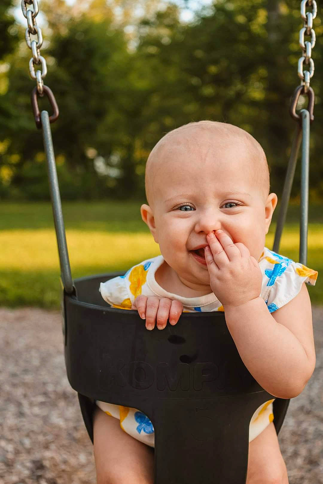 Quinn is registered to the contest to win money with this photo: baby, baby_toddler_clothing, cheek, eye, face, finger, gesture, grass, happy, head, leisure, person, photograph, plant, playground, recreation, skin, swing, toddler, tree