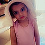 child, girl, hat, pink_clothing, shorts, indoor, floor, expression, face, person, standing, curious, large_eyes, sunhat, casual, young, portrait, home, soft_lighting, toy