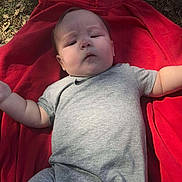 Brighton joined the competition — help win amazing prizes! baby, infant, child, red_blanket, grey_onesie, outdoor, grass, leaves, person, face, arm, leg, clothing, lying_down, curious_expression, sunlight, nature, casual, skin, head