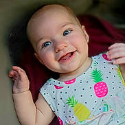 Janie joined the competition — help win amazing prizes! baby, infant, child, smiling, portrait, close_up, blue_eyes, waving, lying_down, colorful_clothing, fruit_pattern, pineapple, strawberry, onesie, happy, face, hands, indoor, candid, cute