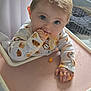 Bonnie-Mae is registered to the contest to win money with this photo: baby, high_chair, snack, eating, blue_eyes, onesie, lion_pattern, hand, face, indoor, lamp, window, table, floor, home_decor, curtain, photography, child, cute, messy