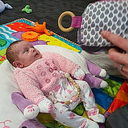 Bonnie-Mae joined the competition — help win amazing prizes! baby, carpet, child, colorful, cozy, curious, cute, floor, hand, indoor, infant, looking, lying_down, pajamas, patterned_clothing, person, pink_clothing, play_mat, soft_toy, toy
