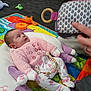 baby, carpet, child, colorful, cozy, curious, cute, floor, hand, indoor, infant, looking, lying_down, pajamas, patterned_clothing, person, pink_clothing, play_mat, soft_toy, toy