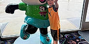 Kaesen is registered to the contest to win money with this photo: boy, carpet, child, clothing, colorful, floor, indoor, light, panda, peace_sign, person, play_area, pose, rain, shoes, sign, smile, statue, toy, window