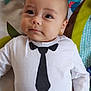baby, infant, child, face, eyes, clothing, onesie, tie_print, bowtie_print, hand, blanket, pattern, colorful, lying_down, portrait, cute, soft_light, indoors, person, young_child