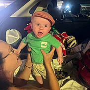 Maverick is registered to the contest to win money with this photo: baby, child, woman, car_trunk, cap, green_shirt, smile, happy, playing, holding, person, indoor, phone, bag, clothing, headwear, expression, casual, interaction, family