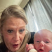 Maverick is registered to the contest to win money with this photo: adult, baby, casual, child, closeup, curious, curtain, expression, face, family, hand, holding, indoor, natural_light, person, portrait, selfie, skin, surprised, woman