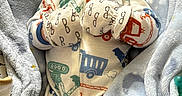 Jayce is registered to the contest to win money with this photo: baby, infant, child, portrait, lying_down, blanket, swaddled, pajamas, mittens, clothing, vehicle_pattern, truck, train, cozy, indoor, close_up, face, wide_eyed, cute, photography