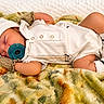 baby, infant, sleeping, pacifier, white_outfit, hat, socks, blanket, bed, portrait, close_up, indoors, lying_down, peaceful, cozy, soft_texture, patterned_blanket, newborn, resting, photography