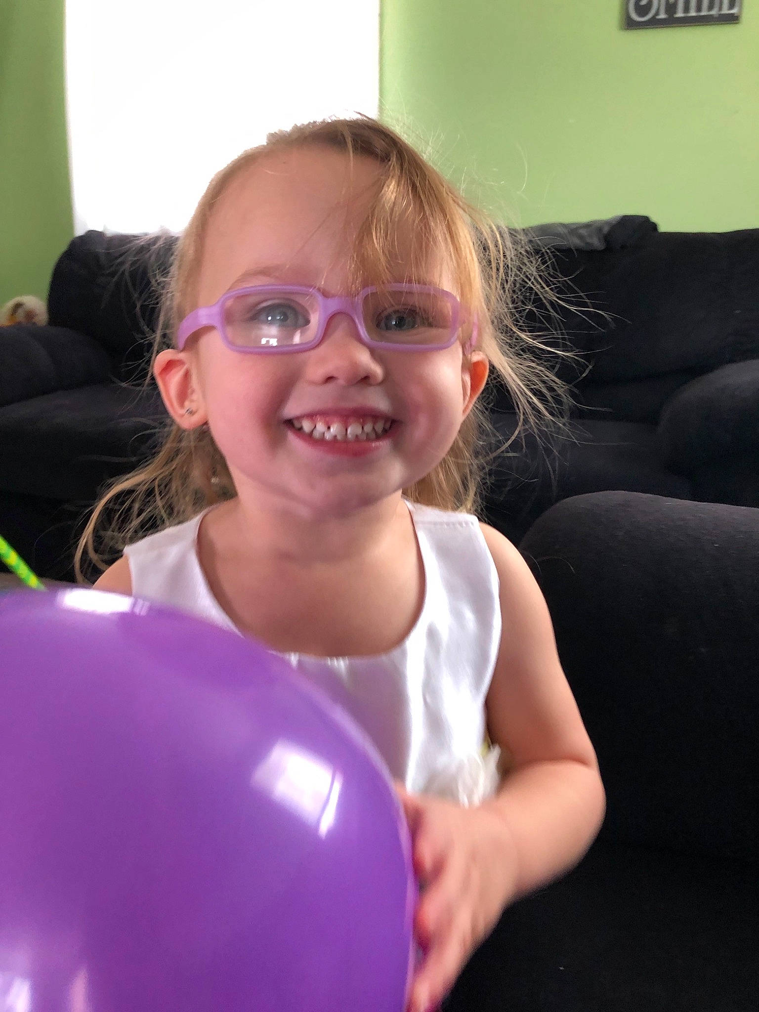 Kaydence is registered to the contest to win money with this photo: balloon, blond, child, ear, eyewear, face, facial_expression, fun, glasses, happy, head, joy, leisure, party_supply, person, purple, smile, toddler