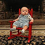 baby, child, rocking_chair, denim_overalls, socks, indoor, fireplace, stone_wall, rug, expression, seated, furniture, home, curious, infant, clothing, patterned_shirt, wood, floor, portrait