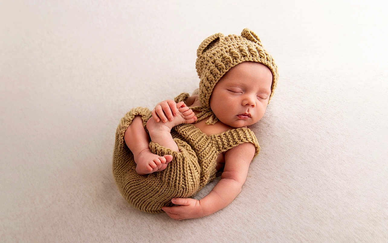 Ronnie is registered to the contest to win money with this photo: baby, newborn, sleeping, knitted_clothing, hat, bear_ears, infant, cute, peaceful, soft_texture, blanket, portrait, small_hands, small_feet, resting, cozy, child, one_person, indoor, closeup