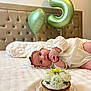 baby, balloon, bed, blanket, blue_eyes, bonnet, bracelet, cake, celebration, cupcake, flower_topping, flowers, headboard, heart_balloon, infant, number_5_balloon, party, portrait, tufted_headboard, white_dress