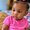 baby, infant, child, portrait, close_up, face, hair_bows, pink_clothing, pink, curly_hair, dark_skin, side_eye, pouting, sitting, indoor, home, shallow_depth_of_field, soft_lighting, photography, cute