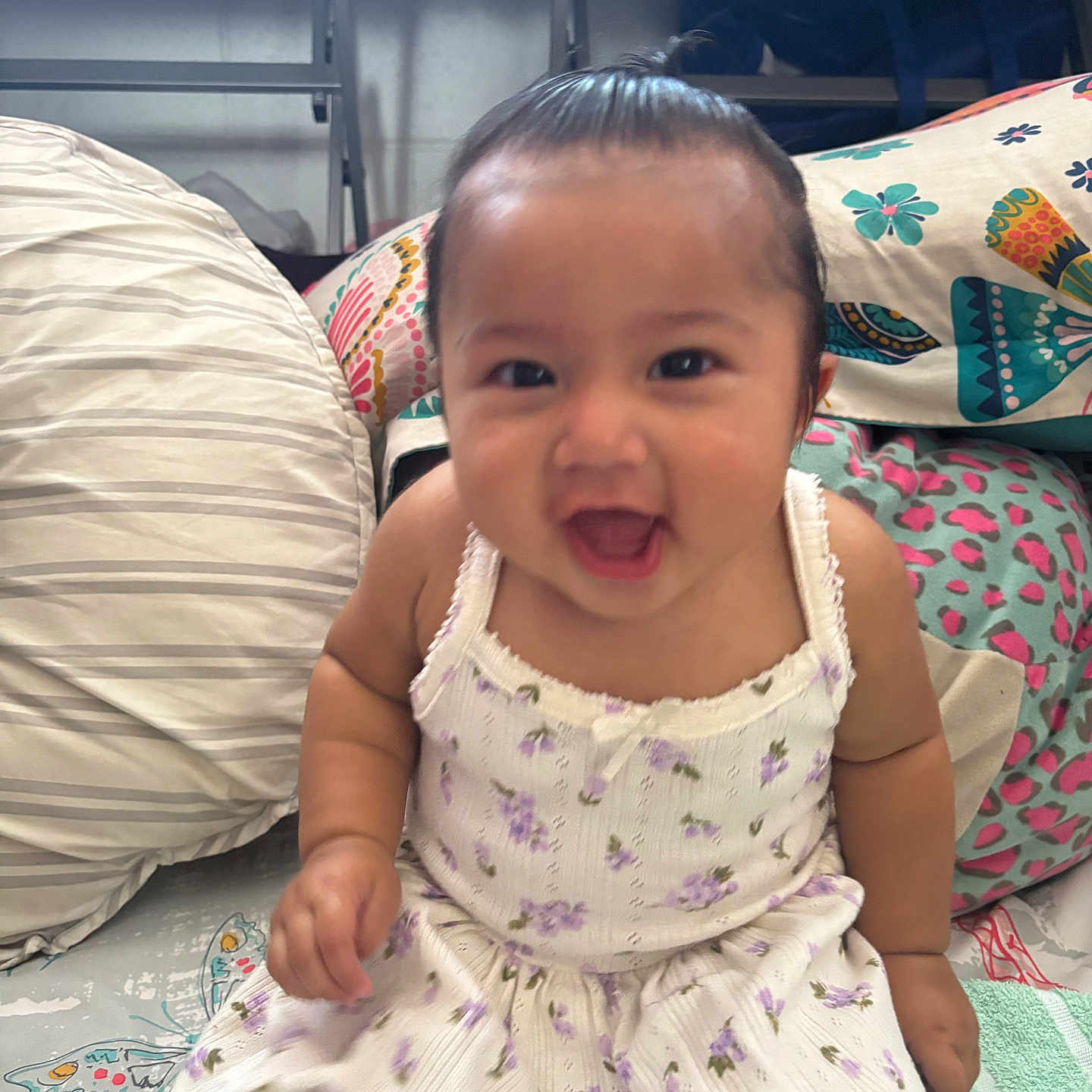 Remedyrose Garcia joined the competition — help win amazing prizes! baby, child, smiling, dress, sitting, pillow, blanket, indoor, cute, happy, infant, person, face, head, patterned, colorful, fabric, clothing, young, playful