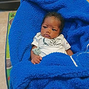 Bryan is registered to the contest to win money with this photo: baby, blanket, blue_blanket, infant, pacifier, clothing, person, face, hand, indoors, floor, expression, portrait, resting, toddler, cute, warm, soft, cozy, child