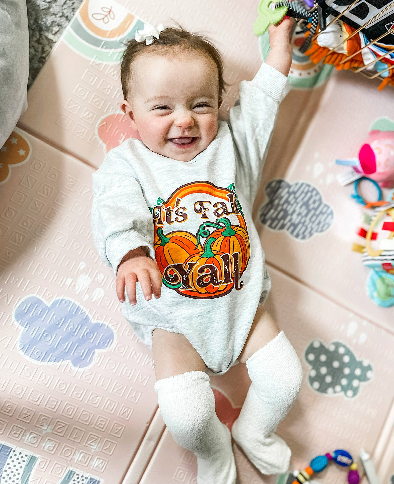 Kora is registered to the contest to win money with this photo: arm, baby, baby_toddler_clothing, child, comfort, finger, happy, human_leg, infant_bodysuit, knee, linens, neck, pattern, person, sleeve, smile, t_shirt, textile, thigh, toddler