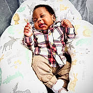 Oneal joined the competition — help win amazing prizes! baby, infant, smiling, plaid_shirt, beige_pants, white_socks, animal_print, pillow, cozy, comfortable, happy, cute, child, indoor, portrait, seated, soft_fabric, patterned, nursery, relaxed
