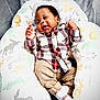 baby, infant, smiling, plaid_shirt, beige_pants, white_socks, animal_print, pillow, cozy, comfortable, happy, cute, child, indoor, portrait, seated, soft_fabric, patterned, nursery, relaxed