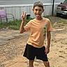 child, boy, peace_sign, tongue_out, outdoor, dirt, shorts, tshirt, playful, smile, cheeky, vehicle, chair, grass, trailer_home, casual, young, person, fun, summer