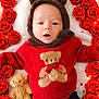 baby, infant, red_sweater, bear_hoodie, teddy_bear, roses, red_roses, flower_arrangement, plush_toy, cute, lying_down, soft_blanket, portrait, child, indoors, warm_clothing, adorable, looking_up, cozy, holiday_theme
