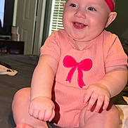 Everleigh is registered to the contest to win money with this photo: baby, smiling, headband, pink_clothing, bow, infant, sitting, bed, indoors, window, blinds, happy, child, cute, human, person, skin, feet, hand, room