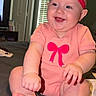 baby, smiling, headband, pink_clothing, bow, infant, sitting, bed, indoors, window, blinds, happy, child, cute, human, person, skin, feet, hand, room