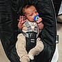 baby, infant, pacifier, baby_rocker, black, striped_pants, beige_top, baby_clothing, indoor, child, cute, person, seatbelt, baby_seat, newborn, small_hands, small_feet, resting, holding, comfort