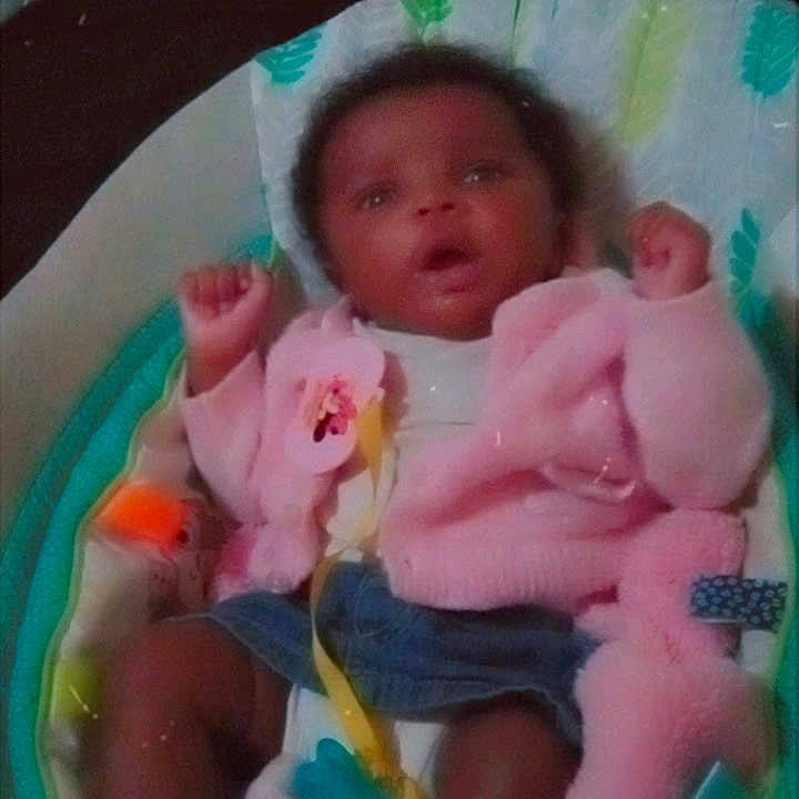 Harmony is registered to the contest to win money with this photo: baby, infant, pink_jacket, denim_shorts, baby_seat, cushion, toy, curly_hair, raised_arms, indoor, blanket, comfort, child, portrait, expression, clothing, seat, baby_accessory, soft_toys, greeting_text