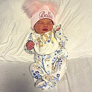 Bella is registered to the contest to win money with this photo: baby, newborn, sleeping, hat, pink, pom_poms, floral_clothing, bib, blanket, soft, cute, infant, child, lying_down, peaceful, indoors, portrait, clothing, face, person