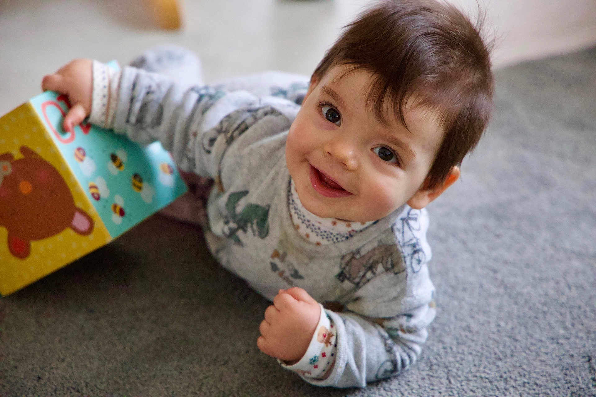 Sacha a rejoint le concours — aidez-le/la à gagner de superbes lots ! baby, child, smiling, face, book, toy, carpet, indoors, pajamas, hand, eyes, cute, happy, portrait, infant, young_child, play, colorful, animal_illustration, cozy