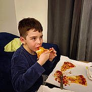 Petru Maria participe au concours pour gagner de l'argent avec cette photo : child, boy, pizza, food, eating, indoor, couch, blue_sweater, fork, pizza_box, curtains, casual, meal, snack, relaxed, young, face, hands, table, cheese