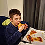 child, boy, pizza, food, eating, indoor, couch, blue_sweater, fork, pizza_box, curtains, casual, meal, snack, relaxed, young, face, hands, table, cheese