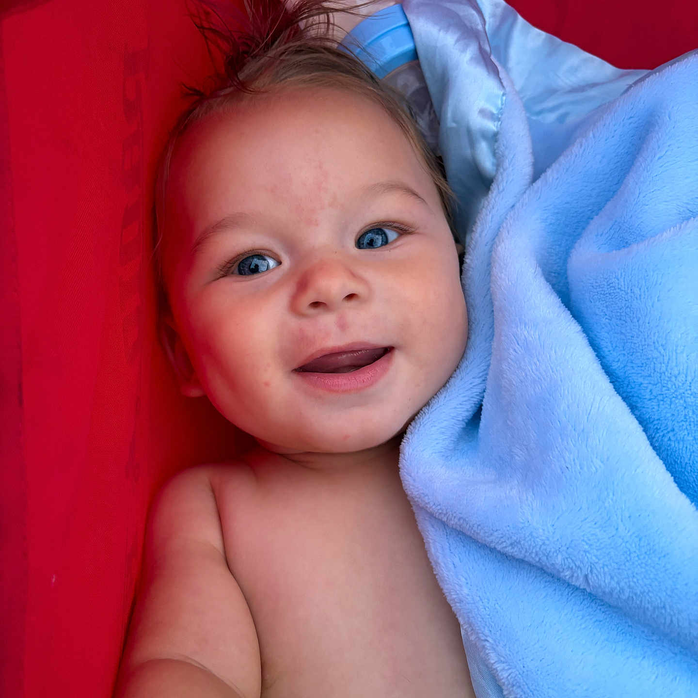 Kasen is registered to the contest to win money with this photo: baby, child, smiling, blue_eyes, blanket, red_background, happy, face, skin, arm, closeup, portrait, infant, cute, soft_texture, lying_down, baby_bottle, hair, indoors, toddler