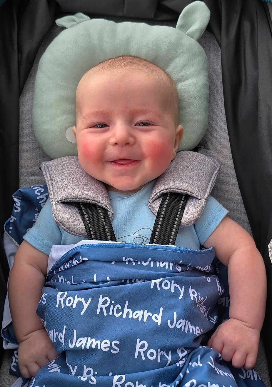 Rory is registered to the contest to win money with this photo: baby, smiling, blanket, blue_blanket, stroller, child, infant, face, head, rosy_cheeks, clothing, cushion, straps, person, happy, sitting, comfort, cute, portrait, baby_boy
