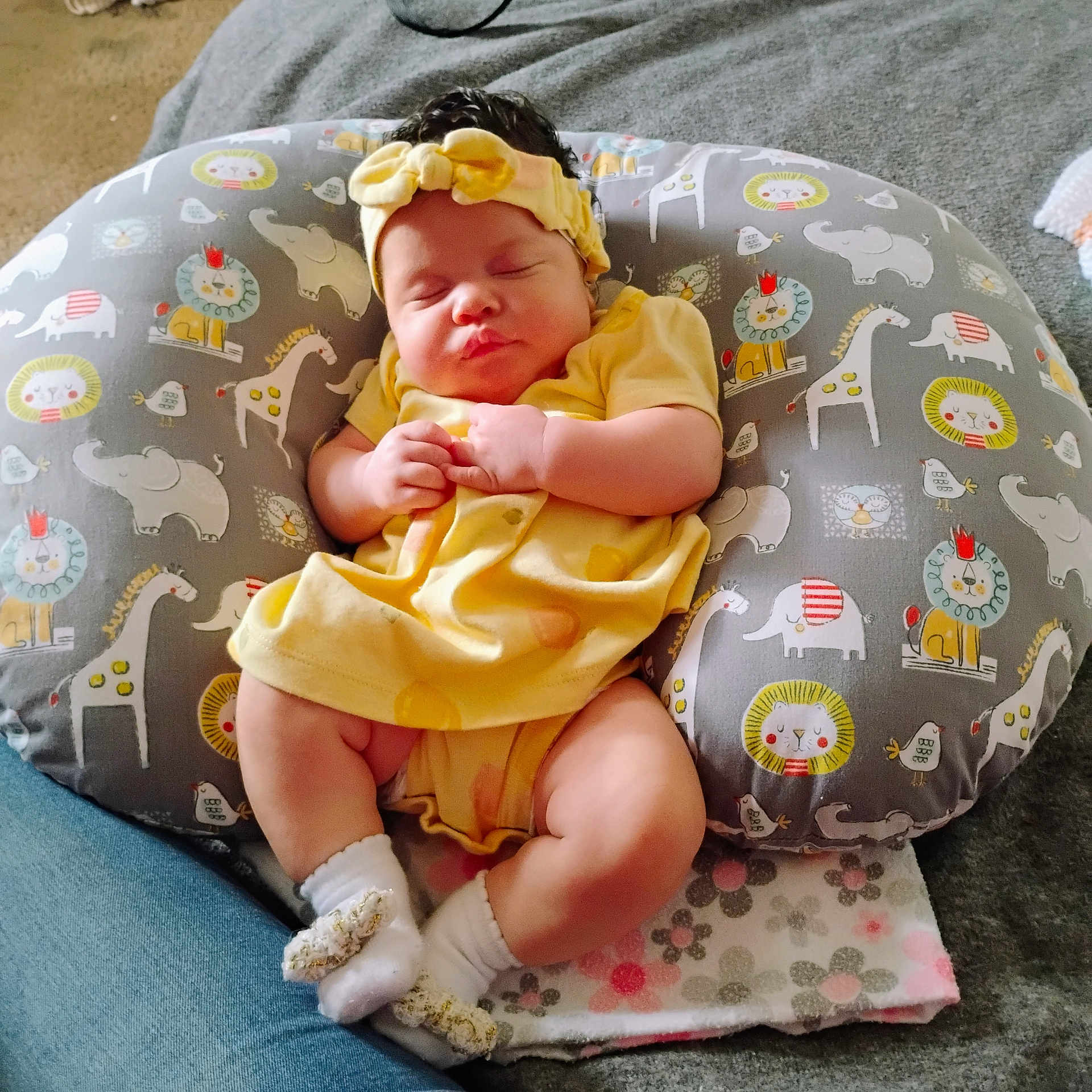 Trinity is registered to the contest to win money with this photo: baby, infant, sleeping, child, headband, yellow_outfit, pillow, patterned_pillow, lion_pattern, elephant_pattern, giraffe_pattern, blanket, socks, feet, hands, closed_eyes, newborn, indoor, carpet, cute