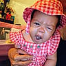 baby, child, infant, hat, dress, red_and_white, checkered, hand, person, face, expression, indoor, home, furniture, decor, cute, portrait, skin, holding, winking