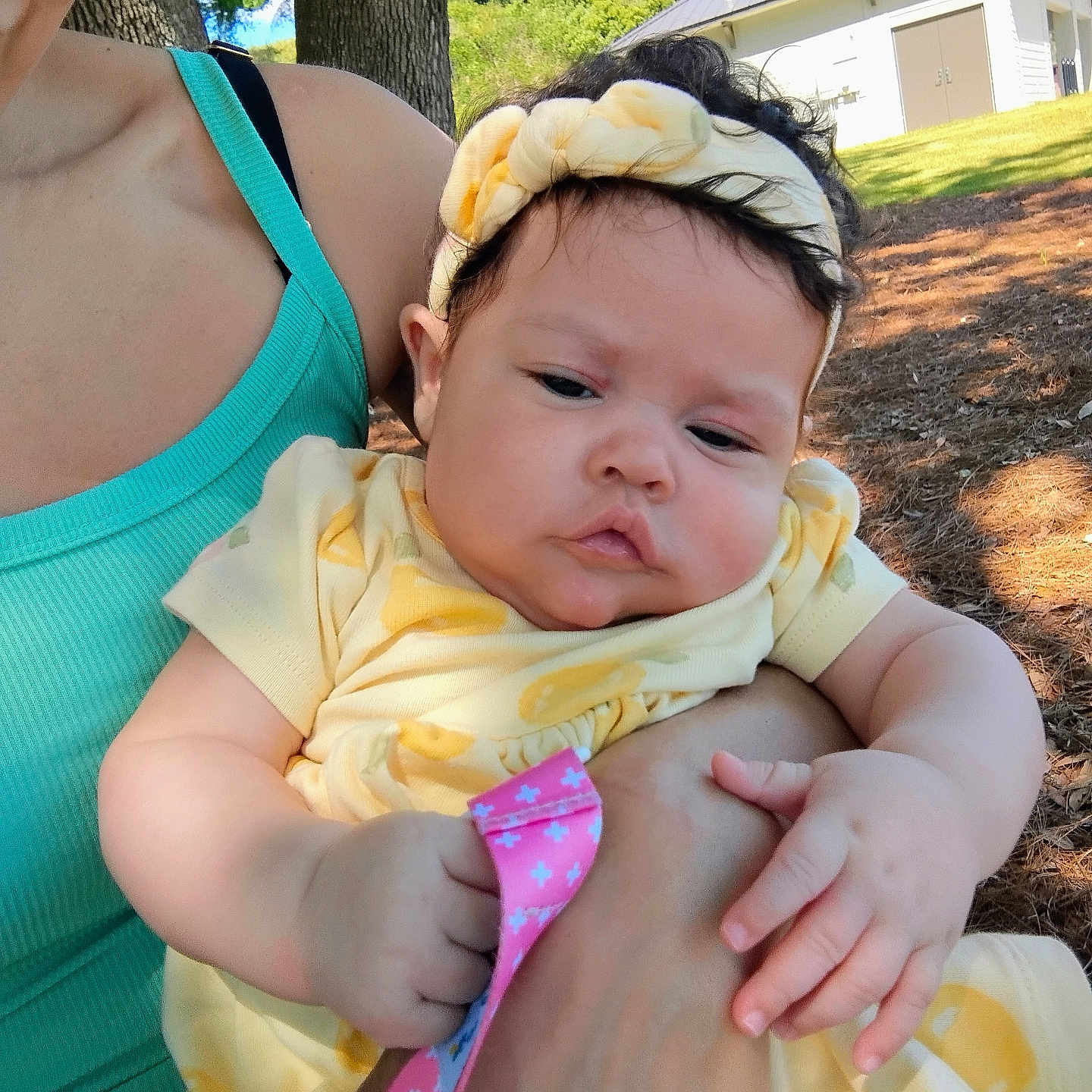 Trinity is registered to the contest to win money with this photo: baby, building, child, curious, cute, daytime, grass, hand, headband, holding, infant, nature, outdoor, person, skin, sunlight, tank_top, tree, woman, yellow_clothing