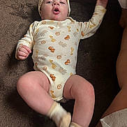 Emmett Sherwood is registered to the contest to win money with this photo: baby, infant, onesie, hat, socks, animal_print, child, cute, soft_surface, brown_background, playful, motion, young_child, indoor, person, portrait, legs, arms, headwear, expression